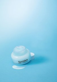 Torriden DIVE IN rauhoittava voide kirkkaassa purkissa, jossa on valkoinen kansi. Vaaleansininen voide, jolla on sileä koostumus, lisänä pieni kermatippa.