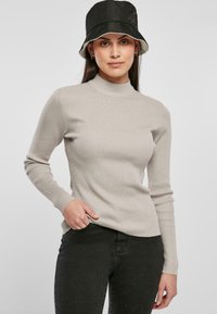 Beige ribbatut turtleneck paita, jossa on pitkät hihat, valmistettu pehmeästä materiaalista, yhdistetty mustiin farkkuihin ja mustaan ämpärilippikseen.