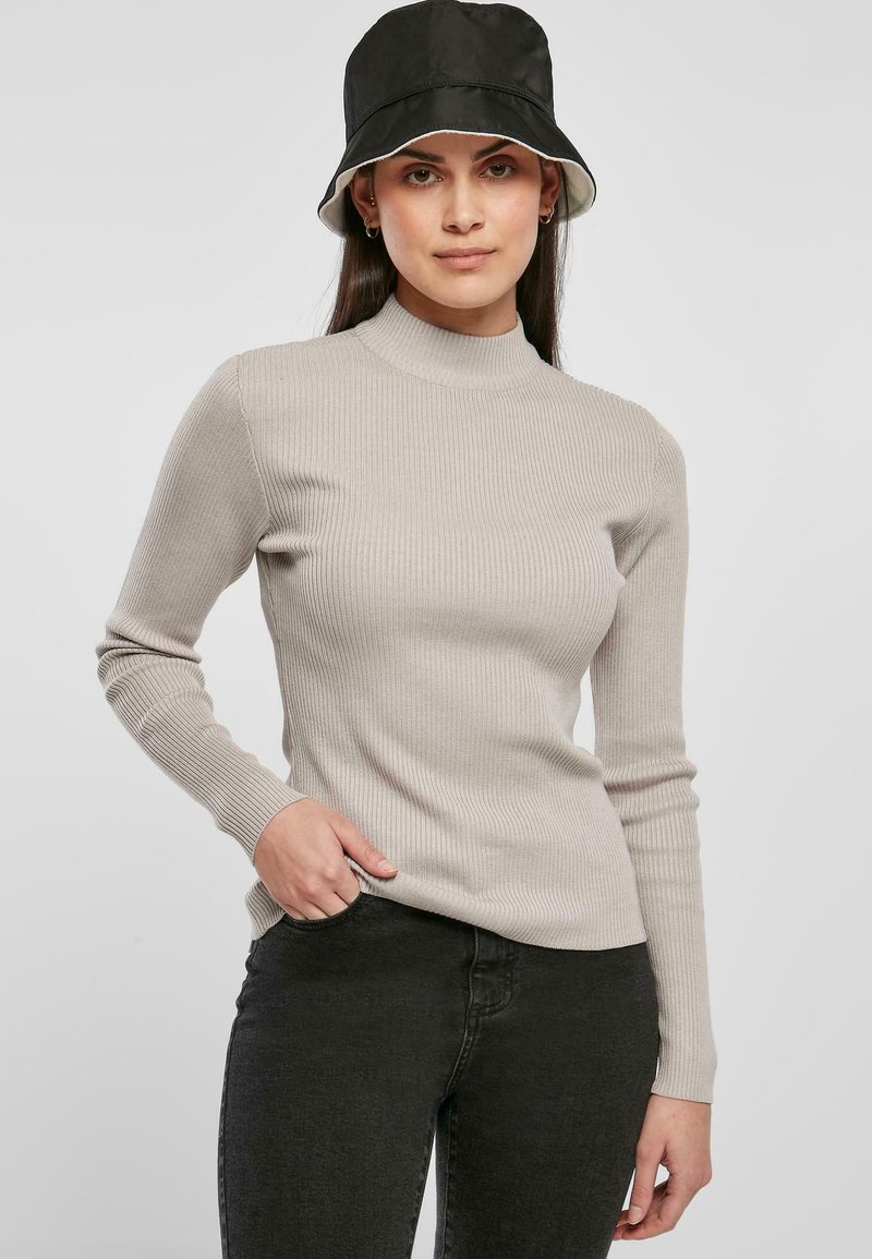 Beige ribbet turtleneck sweater med lange ærmer, lavet af et blødt materiale, parret med sorte jeans og en sort bucket hat.