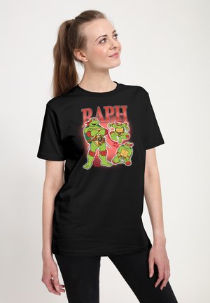 Femme portant un t-shirt noir avec trois personnages des Tortues Ninja adolescents étiquetés "RAPH" en texte rouge sur le devant.