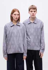 Γκρι σακάκια με κάθετες ρίγες και φερμουάρ στο μπροστινό μέρος, με γιακά και μακριά μανίκια, συνδυασμένα με σκουρόχρωμο τζιν παντελόνι.