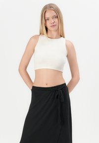 Hvid ribbet crop top med høj hals, sammen med en sort indpakningsskørt med en bundet talje. Glat stof og minimalistisk design.