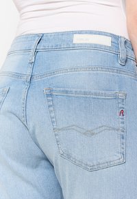 Lichtblauwe denimjeans met een strakke pasvorm, voorzien van een wit label en een rode 'R' accent op de achterzak.