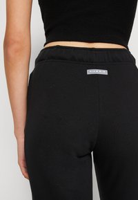 Juodos Nike Air sportinės kelnės su elastinga juosmens juosta ir logotipo panele; pagamintos iš lygaus, minkšto audinio; prigludusi forma.