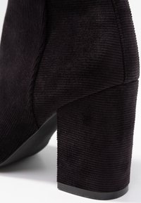 Stivale alla caviglia in corda nera con punta rotonda e tacco quadrato chunky, caratterizzato da una texture a righe e un design elegante.