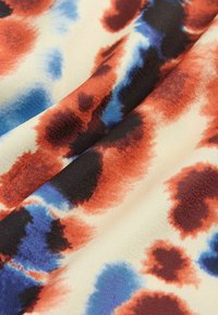 Sträckt tyg med en krämfärgad bakgrund och abstrakta mönster i rödbruna, svarta och blå nyanser, som visar en jämn textur.