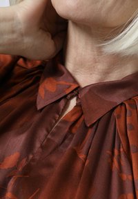 Seidene Bluse in sattem Braun mit floralem und gepunktetem Muster, ausgestattet mit einem Kragenhalsausschnitt und dezenten Falten-details.