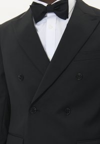 Melns divrinda tuksēts žakets ar satīna picēlana apkakli, atbilstošs melns tauriņš un balta kleita krekls. Strukturēta auduma un sašūts pieguļošs stils.