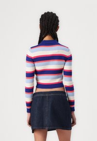 Pull en maille côtelée court avec des rayures horizontales multicolores en bleu, rose et blanc ; possède des manches longues et un col. Associé à une jupe en denim.