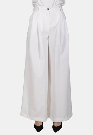 Pantaloni bianchi a vita alta e gamba larga con pieghe anteriori, chiusura con bottone e cerniera, indossati con décolleté nere con punta a spillo.