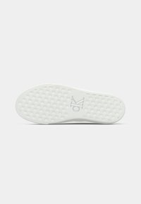Suola di sneaker bianca con motivo intrecciato e logo "CK" impresso al centro, fotografata su uno sfondo semplice.