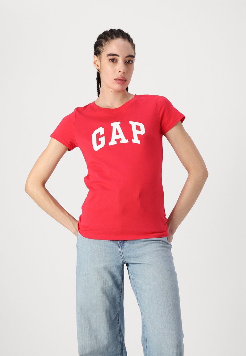 Raudona medvilninė marškinė, su balta "GAP" logotipu, suapvalintu kaklu ir trumpomis rankovėmis, derinama su šviesiai mėlynomis plačiomis džinsomis.