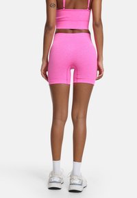 Tight rosa sportcropp-top och shorts gjorda av stretchigt material, med en hög midja och slät textur. Vita sneakers fulländar outfiten.