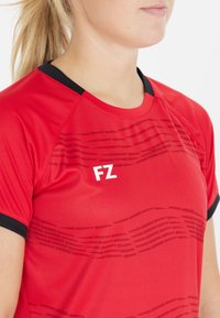 Punainen urheilupaita mustilla yksityiskohdilla, jossa on aaltoilukuosi ja valkoinen "FZ" logo. Valmistettu sileästä, kevyestä materiaalista.
