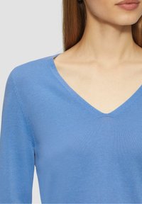 Jasnoniebieski sweter z dekoltem w serek, wykonany z miękkiego, drobno dzianego materiału, z długimi rękawami i gładką teksturą z minimalnymi zdobieniami.