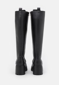 Bottes montantes noires en cuir lisse avec une semelle épaisse, dotées d'une fermeture éclair arrière et de languettes pour faciliter l'enfilage.