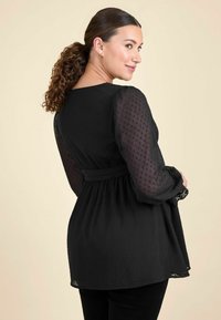 Čierna blúzka s textúrovanými, priehľadnými dlhými rukávmi a čipkovými detailmi. Vyznačuje sa nariaseným pásom a voľným strihom, štýlovo navrhnutá.