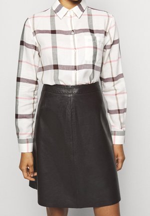 Biała koszula z długim rękawem na guziki z wzorem w kratę w odcieniach szarości, brązu i różu, wpuszczona w czarną spódnicę ze skóry sięgającą do kolan.