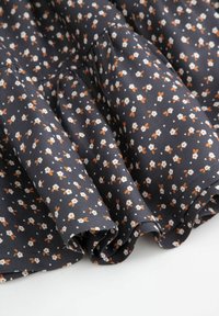 Ciemnogranatowa tkanina z małymi wzorami kwiatowymi w kolorze białym i pomarańczowym, o plisowanej strukturze i miękkim układzie.