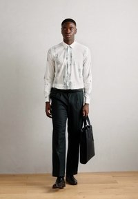 Λευκό πουκάμισο με μακριά μανίκια και γκρίζα αφηρημένα σχέδια, μαύρο παντελόνι και μαύρη τσάντα tote; λείο ύφασμα, κομψή εφαρμογή και μύτες παπούτσια.