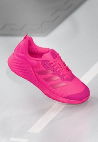 Bright pink athletic sneaker with mesh upper, laces, three side stripes, and textured sole on light gray surface.