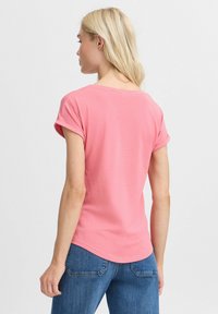 T-shirt rose clair avec des manches courtes retroussées, coupe décontractée et ourlet incurvé. Porté avec un jean bleu, mettant en avant une texture de coton lisse.