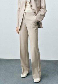 Pantalons beiges ajustés avec une coupe droite, fabriqués en tissu lisse. Comprend des poches avant et une taille mi-haute.