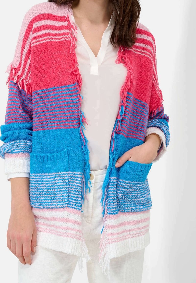 Cardigan multicolore présentant des motifs à rayures roses, bleues et blanches, des bords effilochés et deux poches avant, fabriqué en tissu doux et texturé.