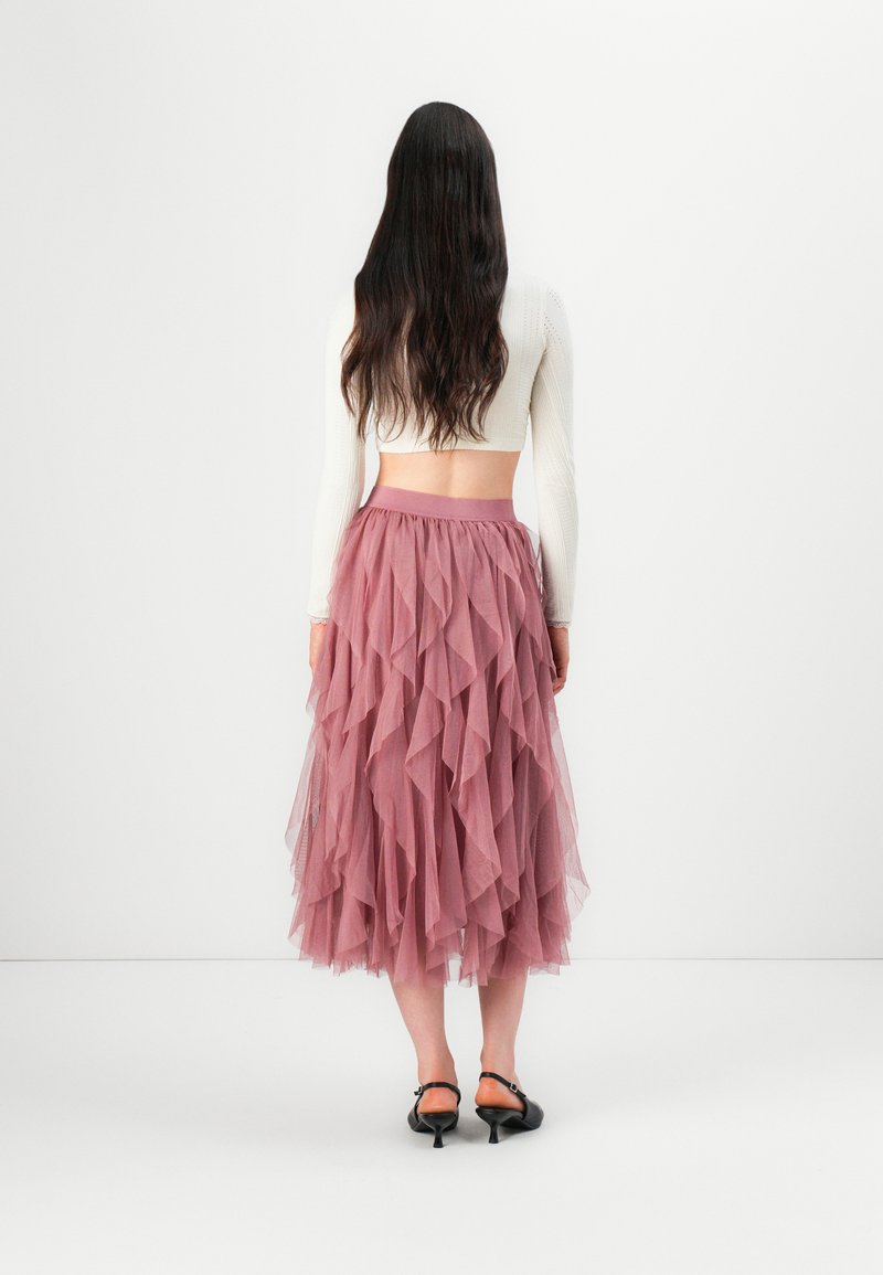 Tüllrock mit geschichteten Rüschen in sanftem Rosa, ausgestattet mit einem breiten, elastischen Bund und kombiniert mit schwarzen Absatzsandalen.