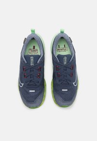 Zapatillas Nike con parte superior de malla azul marino, suela verde, detalles rojos en los cordones y un patrón texturizado en la zona de los dedos.