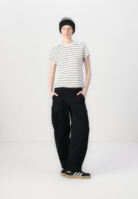 T-shirt a righe bianche e nere, pantaloni cargo neri dal fit rilassato, berretto in maglia nero, sneaker nere con strisce bianche, design semplice e informale.