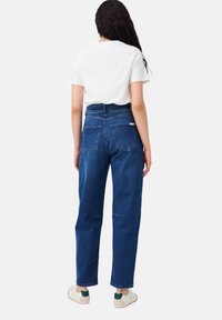 Hochgeschnittene blaue Denim-Jeans mit einer lockeren Passform, ausgestattet mit Gesäßtaschen und einem geraden Bein-Design. Kombiniert mit einem weißen Kurzarmhemd.