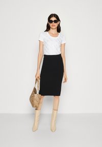 Hvid t-shirt med et subtilt mønster, sort blyantskørt, beige hæl-støvler og en mønstret beige taske. Solbriller fuldender looket.