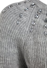 Grauer Strickpullover mit einem strukturierten Muster, geschmückt mit klaren, tropfenförmigen Kristallen entlang der Schulternaht.