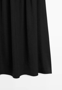 Czarna spódnica w kształcie litery A z miękkimi plisami, do kolan, wykonana z gładkiego materiału, przedstawiona na białym tle.