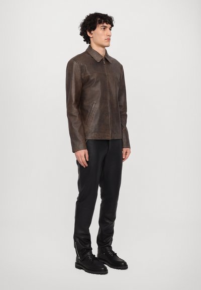 Bruine leren jas met een kraag, rits aan de voorkant en zijzakken. Draag het boven zwarte strakke broek en zwarte veterschoenen. Eenvoudig, gestroomlijnd ontwerp.