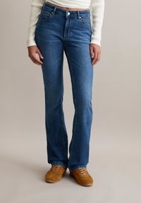 Blaue Denim-Jeans im Straight-Leg-Schnitt mit fünf Taschen, einem Knopfverschluss und dezenten Nähdetails, getragen mit braunen Schnürschuhen.