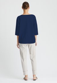 Marineblaues Oberteil mit Dreiviertelärmeln, lockerer Passform und Bootsausschnitt, kombiniert mit hellbeigen, an den Säumen hochgerollten, schmal zulaufenden Hosen.