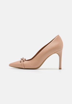 Zapato de tacón alto de piel en color nude con punta afilada y un pequeño lazo decorativo en la parte delantera. Textura lisa y tacón de aguja esbelto.