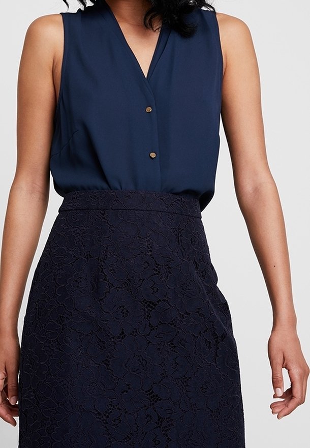 Blusa senza maniche color navy con scollo a V e due bottoni dorati sul davanti, abbinata a una gonna in pizzo color navy con un motivo floreale.