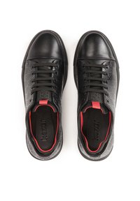Zapatillas negras con una puntera brillante, paneles laterales texturizados con un patrón de logotipos, cordones negros y acentos rojos en el talón y el cuello.