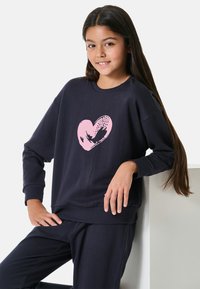 Marinblå sweatshirt med en rosa hjärtgrafik p�å framsidan. Gjord av mjukt material, har långa ärmar och en avslappnad passform. Matchas med tillhörande byxor.