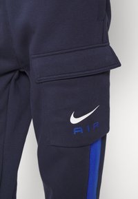 Pantalons de survêtement navy avec une poche cargo latérale, un logo Nike blanc et une bande d'accent bleu. Fabriqués en tissu doux avec une finition lisse.
