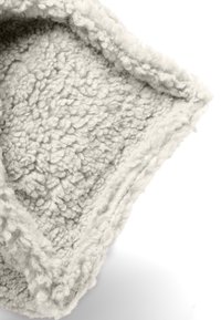 Close-up van zacht, crème-kleurig, textuurstof met dikke, lussen garen en een omgeslagen rand op een witte achtergrond.