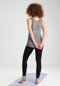 Grijs geribd tanktop gecombineerd met zwarte leggings. Het tanktopje heeft een laag uitgesneden rug, terwijl de leggings aansluitend en naadloos zijn. Ontworpen voor comfort.