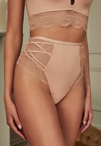 Beige lingerieset met een high-waisted slip met kantaccenten en uitsnijdingen, gecombineerd met een bijpassende bralette met kantafwerking.