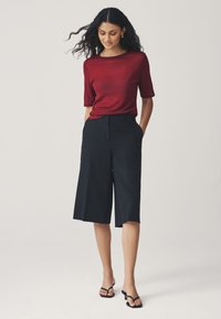 Rød kortærmet top kombineret med sorte, vidde bukser og sorte sandaler. Toppen har en glat, let skinnende tekstur.