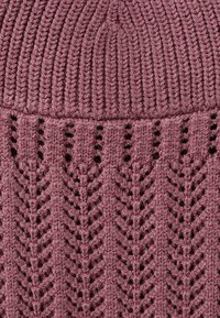 Gros plan sur un tissu tricoté rose poussiéreux avec une section supérieure côtelée et un motif en chevron en dentelle en dessous.