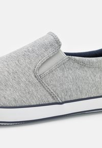Szürke slip-on cipő, textúrált anyagból készült, rugalmas oldalsó panelekkel és fehér gumitalppal, tengerészkék díszítéssel.