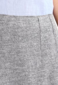 Jupe en laine grise avec une texture douce, dotée d'une taille sans couture et de poches latérales, partiellement visible au-dessus d'une chemise bleu clair.